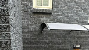 Een stenen muur met een raam, een houten terras en een metalen hekwerk.