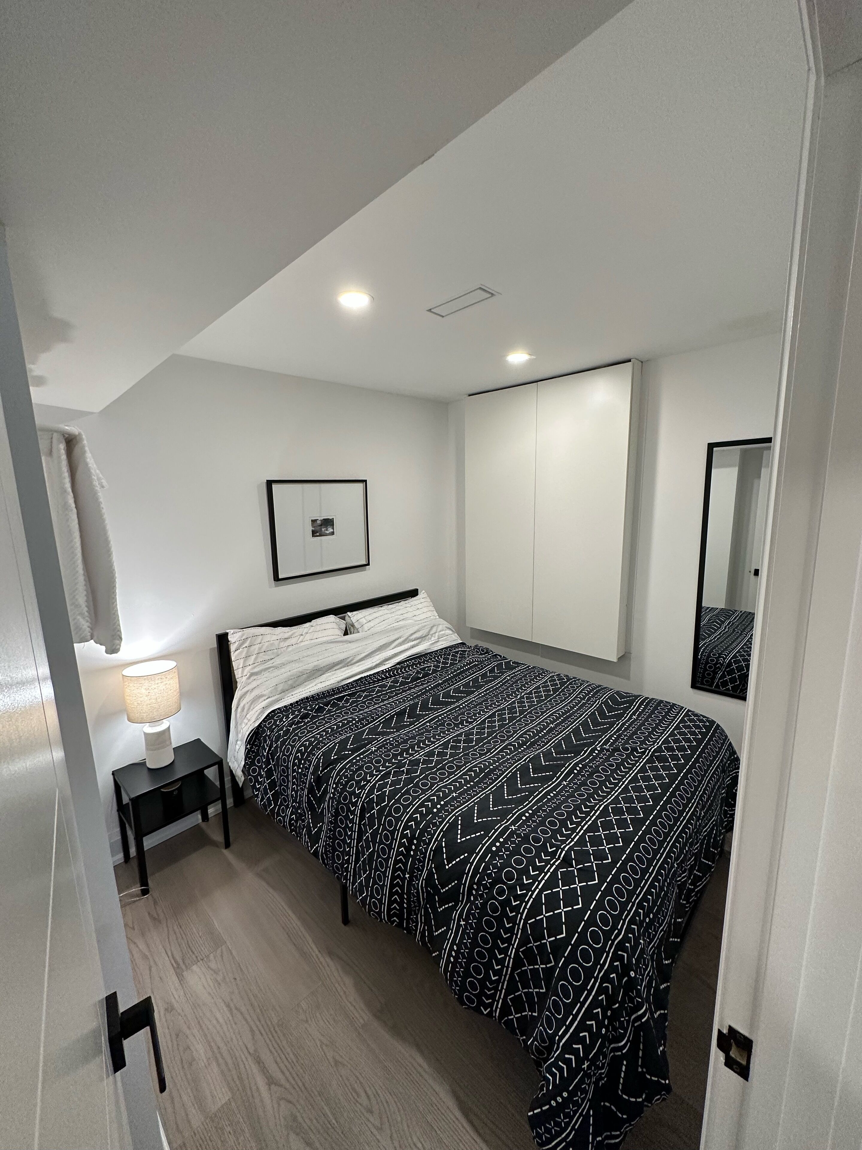 A bedroom with a bed, a nightstand, a wall-mounted TV, a wardrobe, and a mirror.