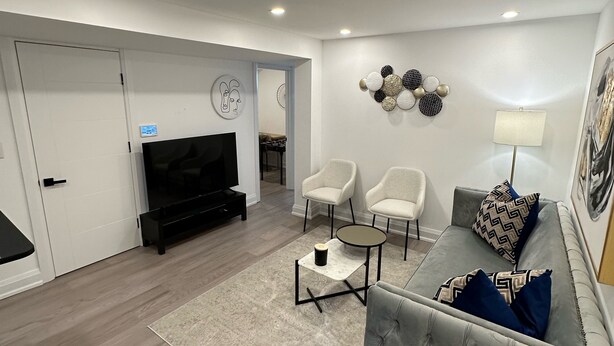 Een moderne woonkamer met een grijze bank, twee witte fauteuils, een zwart tv-meubel en een decoratief wandobject.