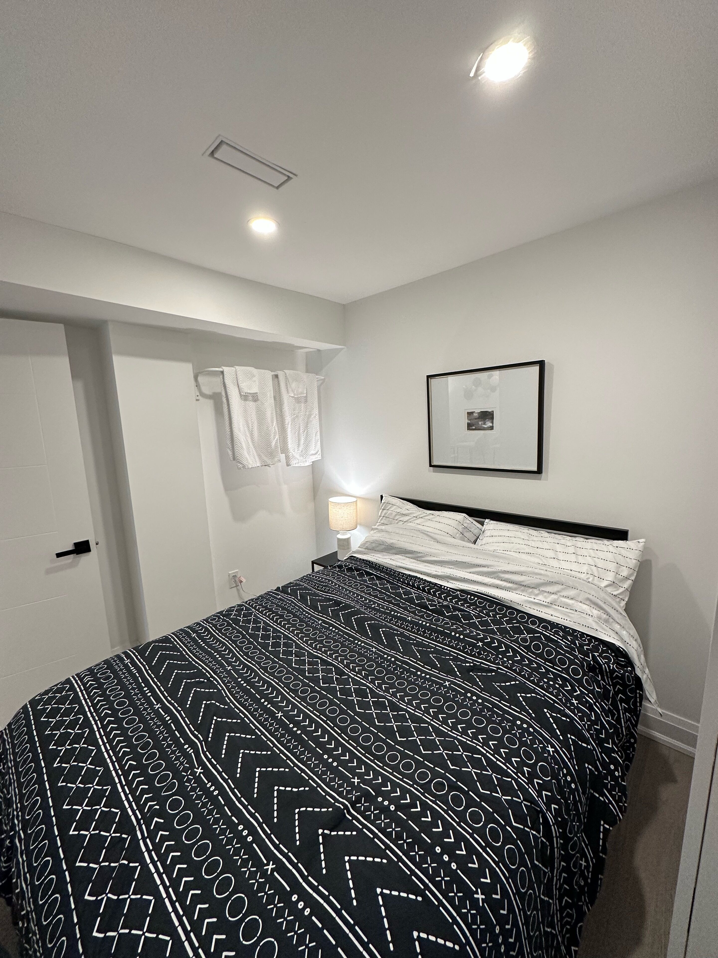 Une chambre à coucher avec un lit, une table de chevet, un tableau accroché au mur et une porte.