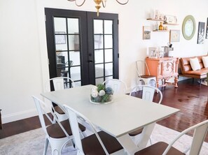 A dining area with a white table and chairs, a black door, and a brown floor.