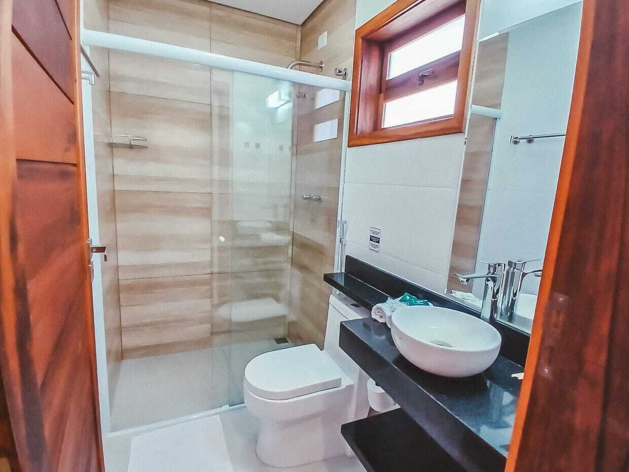 Ein Badezimmer mit Duschkabine aus Glas, einer weißen Toilette und einer schwarzen Ablagefläche mit Waschbecken.