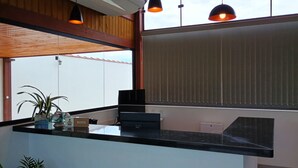 A reception area with a black counter, a plant, a reception desk, and a window with blinds. - Pousada Mirante do Sol (Paraty)