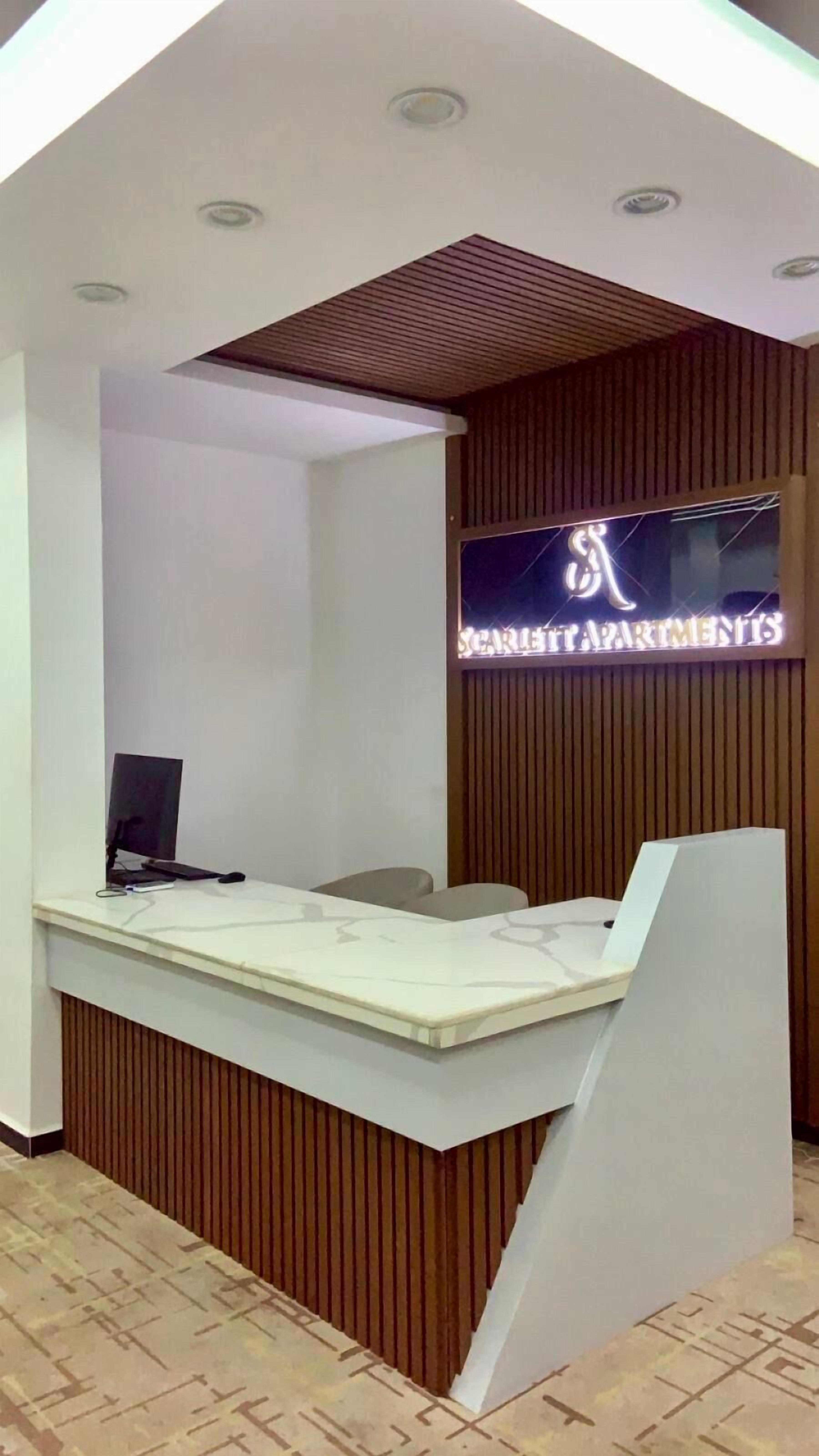 Un mostrador de recepción con diseño de paneles de madera, una computadora y un letrero que dice 'Scarlett Apartments'.