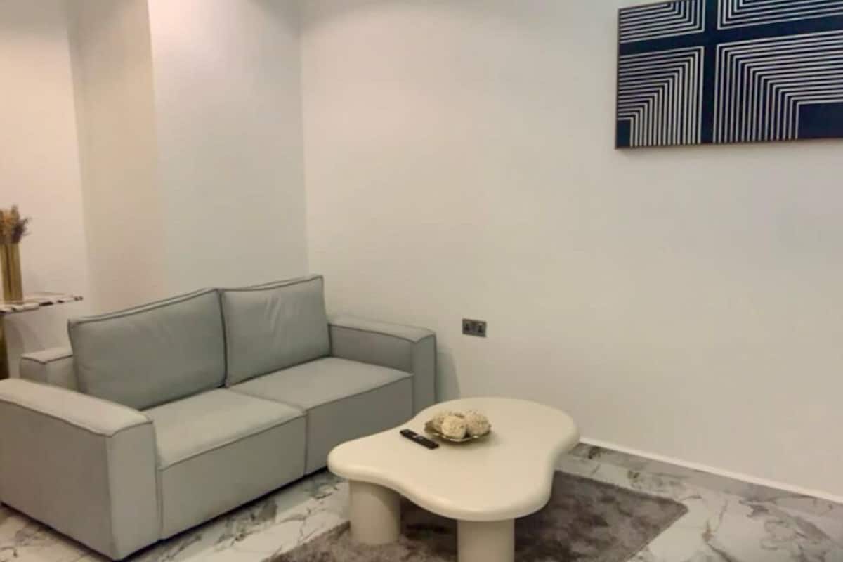 Un salon moderne avec un canapé gris, une petite table basse blanche et un miroir rond accroché au mur.
