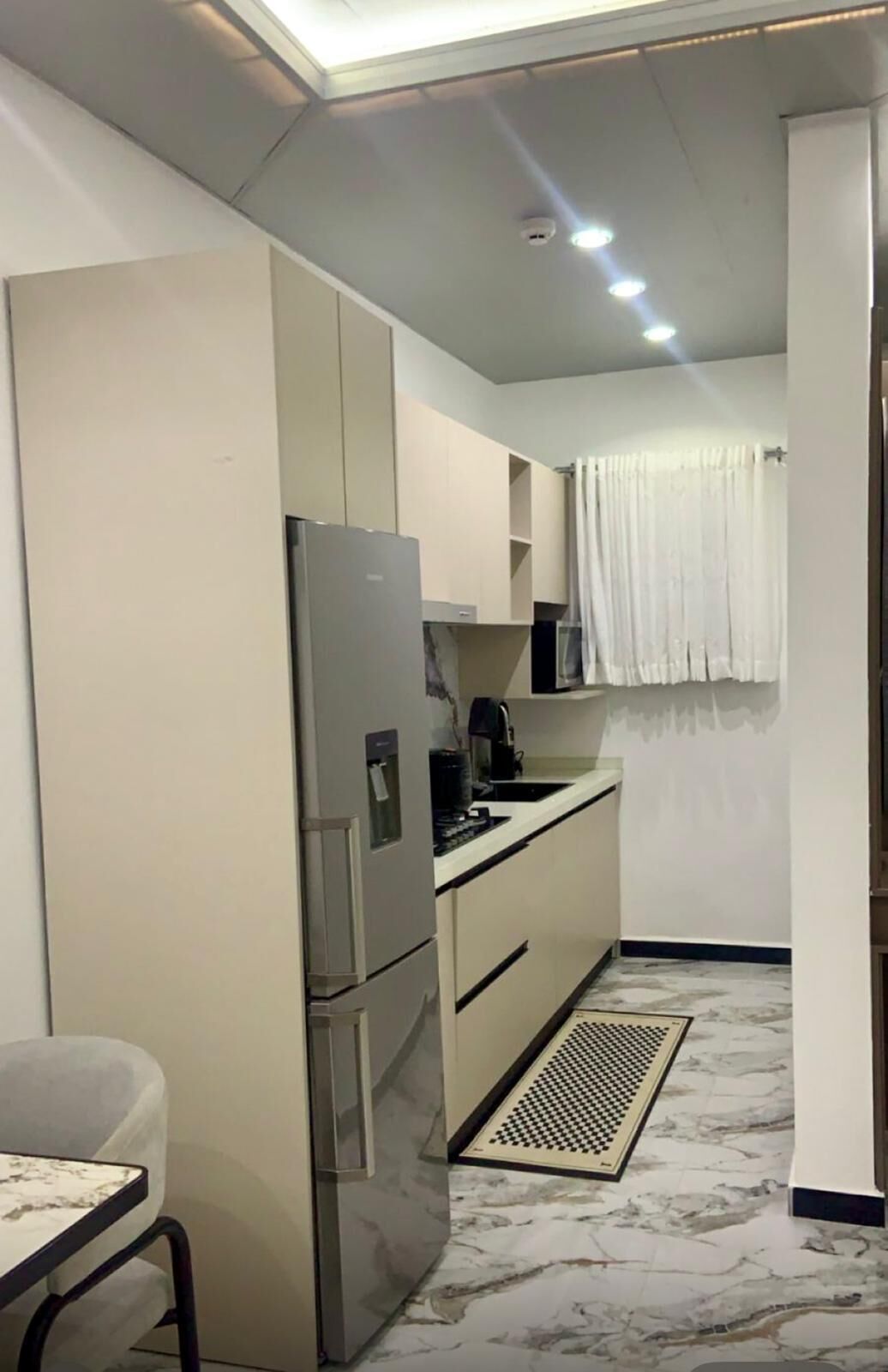 Cocina compacta con refrigerador, microondas, lavamanos y un pequeño comedor con una silla.
