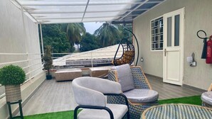 A covered outdoor seating area with wicker furniture, a cushioned sofa, and a small round table. - Scarlett Apartments (Monrovia)