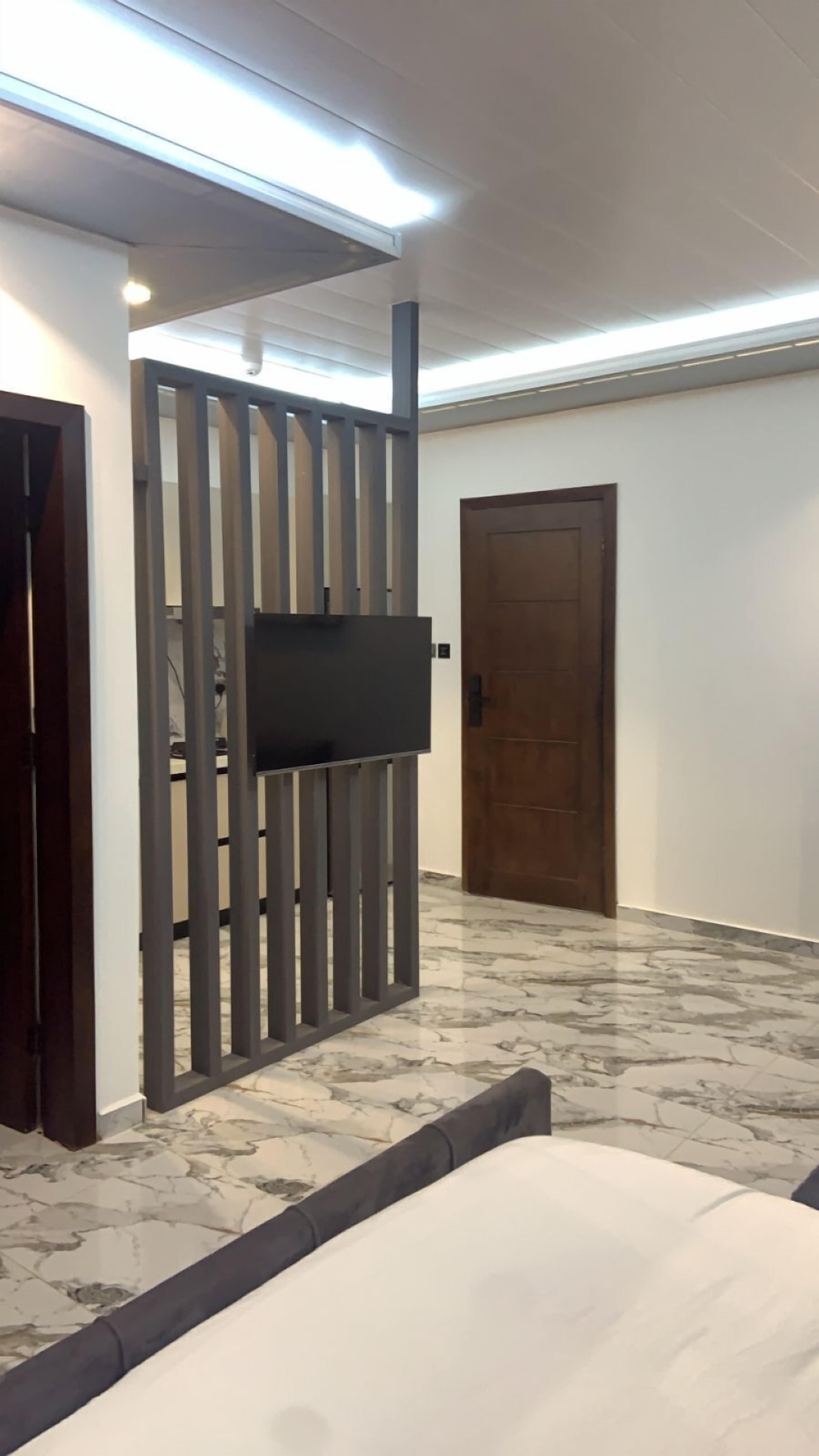 A room with a TV mounted on a grey partition, a wooden door, and a marble floor.