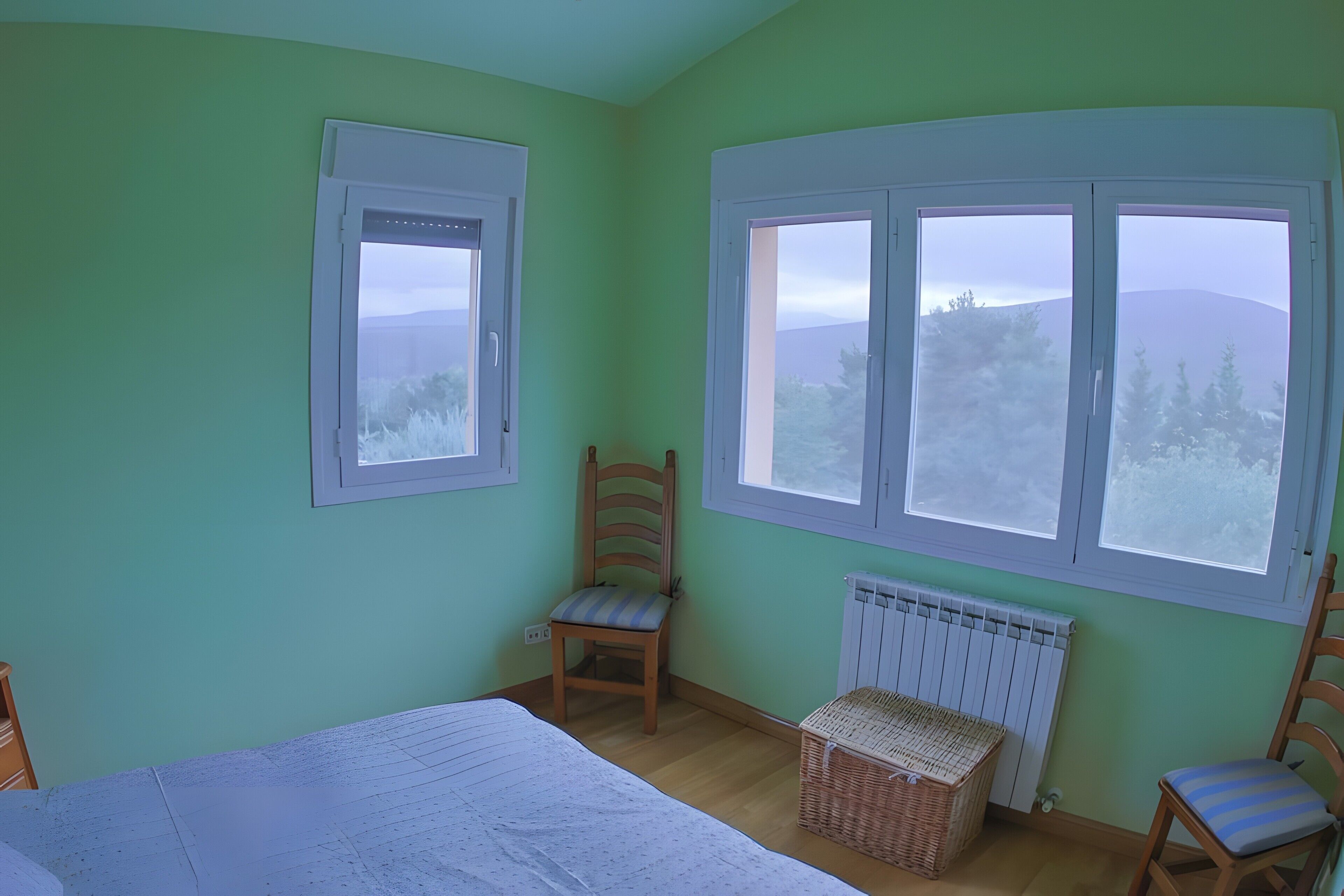 Una habitación con cama, dos sillas, un ventanal con vistas y un radiador.