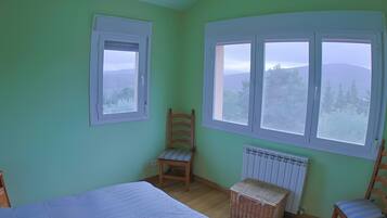 Una habitación con cama, dos sillas, un ventanal con vistas y un radiador.