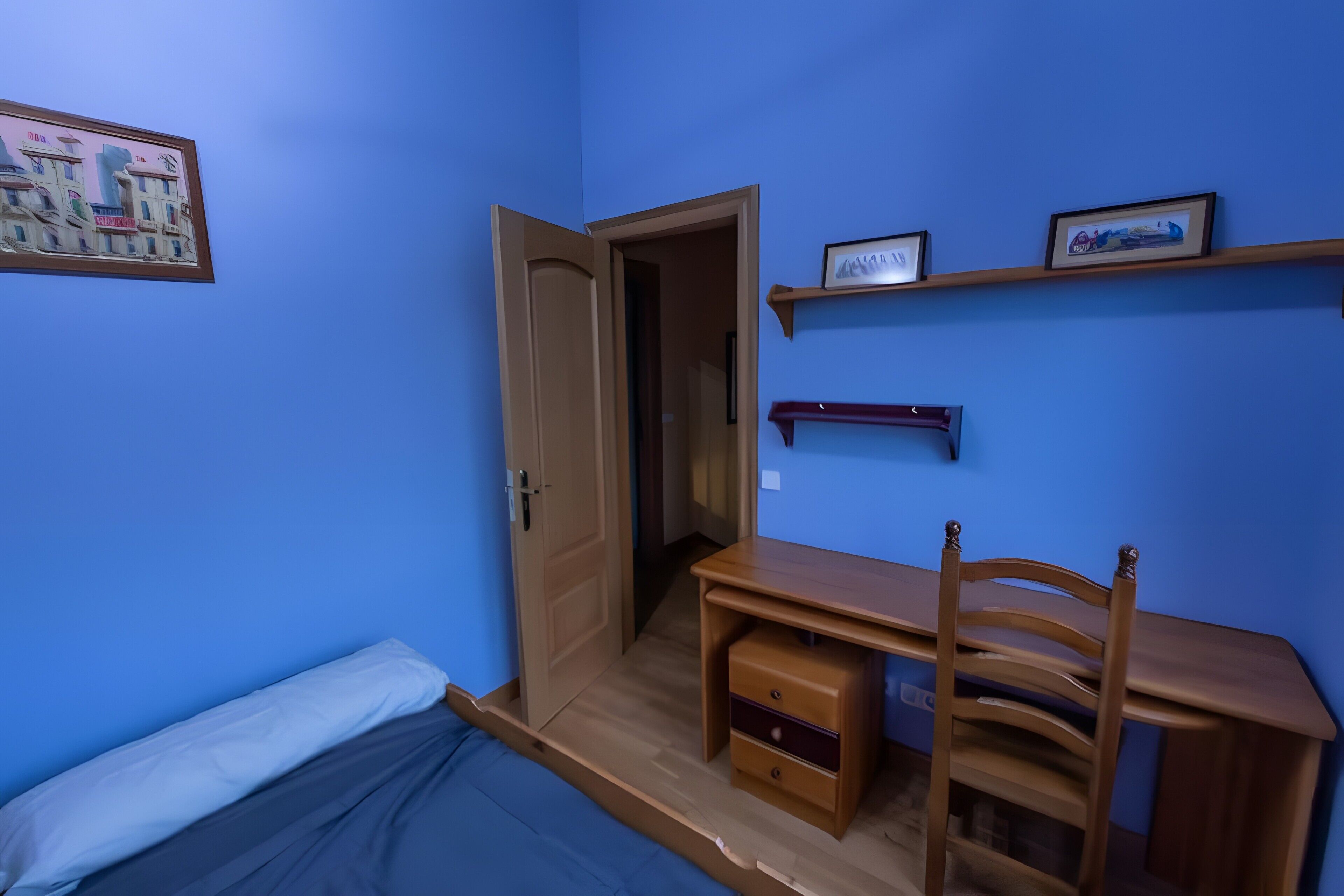 Een kamer met een bed, een bureau, een stoel en een deur naar een andere kamer.