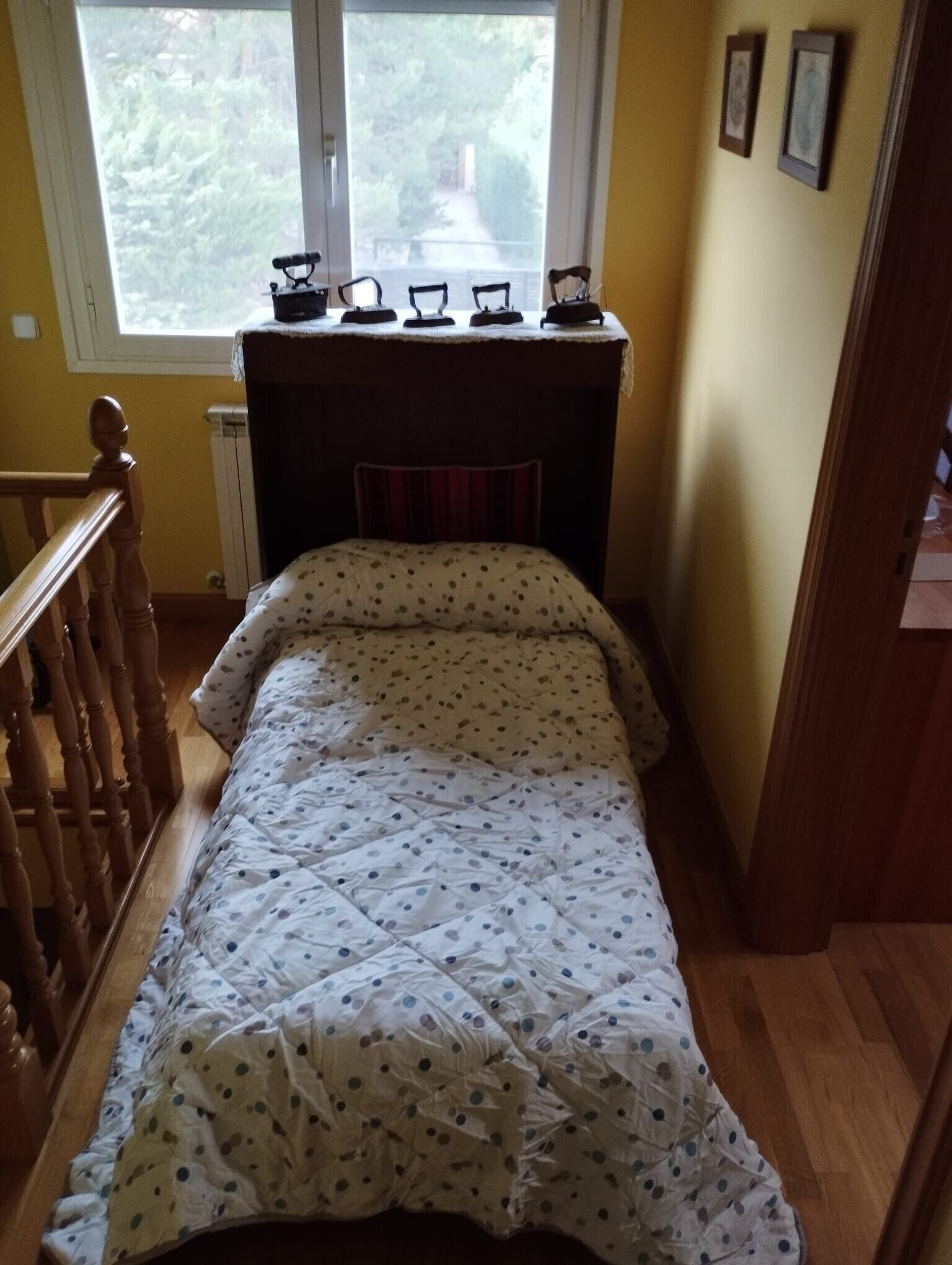 A bedroom with a bed, a window, a radiator, and a wooden staircase.