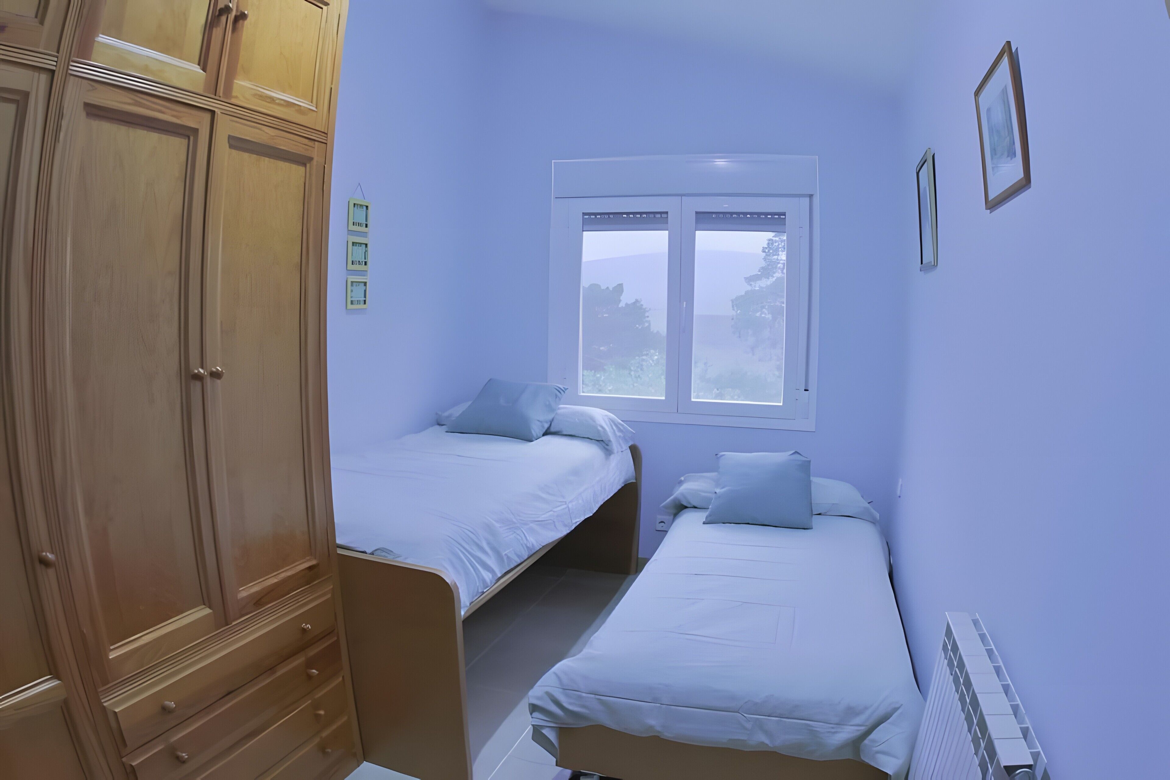 Un dormitorio con dos camas individuales, un armario, una ventana y un radiador.