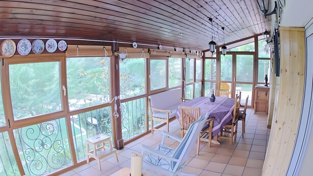 A covered patio with a dining table, chairs, and a view of greenery.