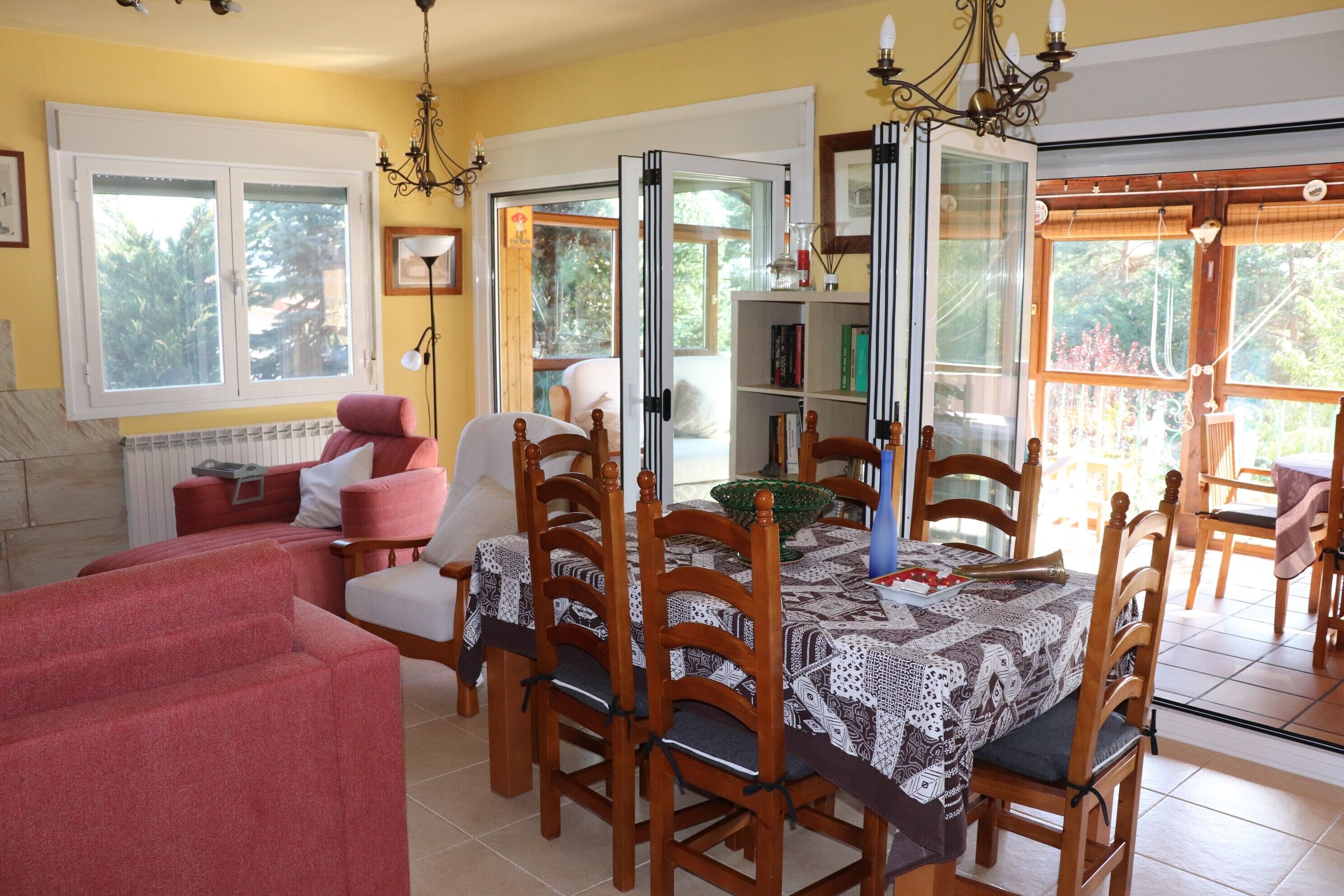 Un comedor con una mesa dispuesta para cuatro personas, rodeada de sillas de madera, un sofá rojo y una estantería.
