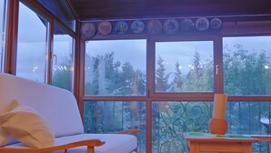 A room with a sofa, a table with a vase, and large windows with a view of trees.