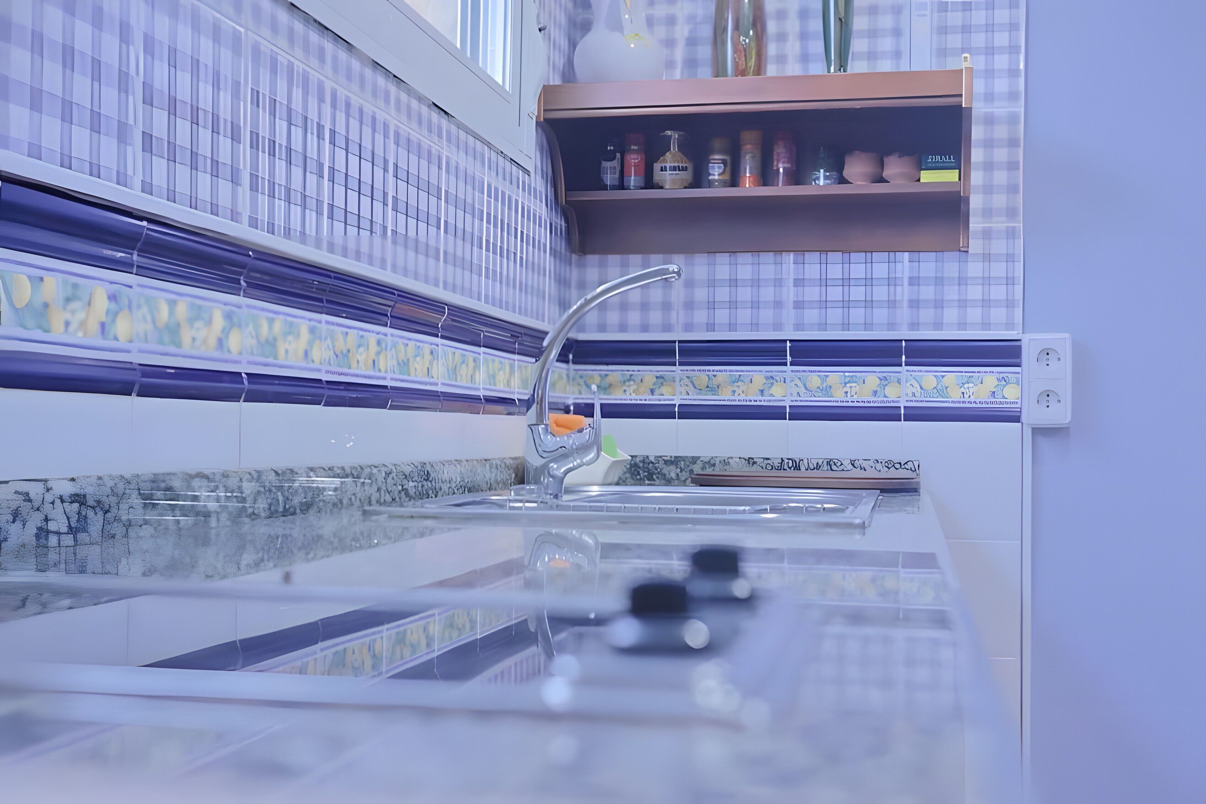 A kitchen with a modern faucet, a tiled backsplash, and a shelf with kitchen items.