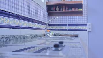 A kitchen with a modern faucet, a tiled backsplash, and a shelf with kitchen items.