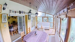 A dining area with a table and chairs, a sofa, and a view through large windows.