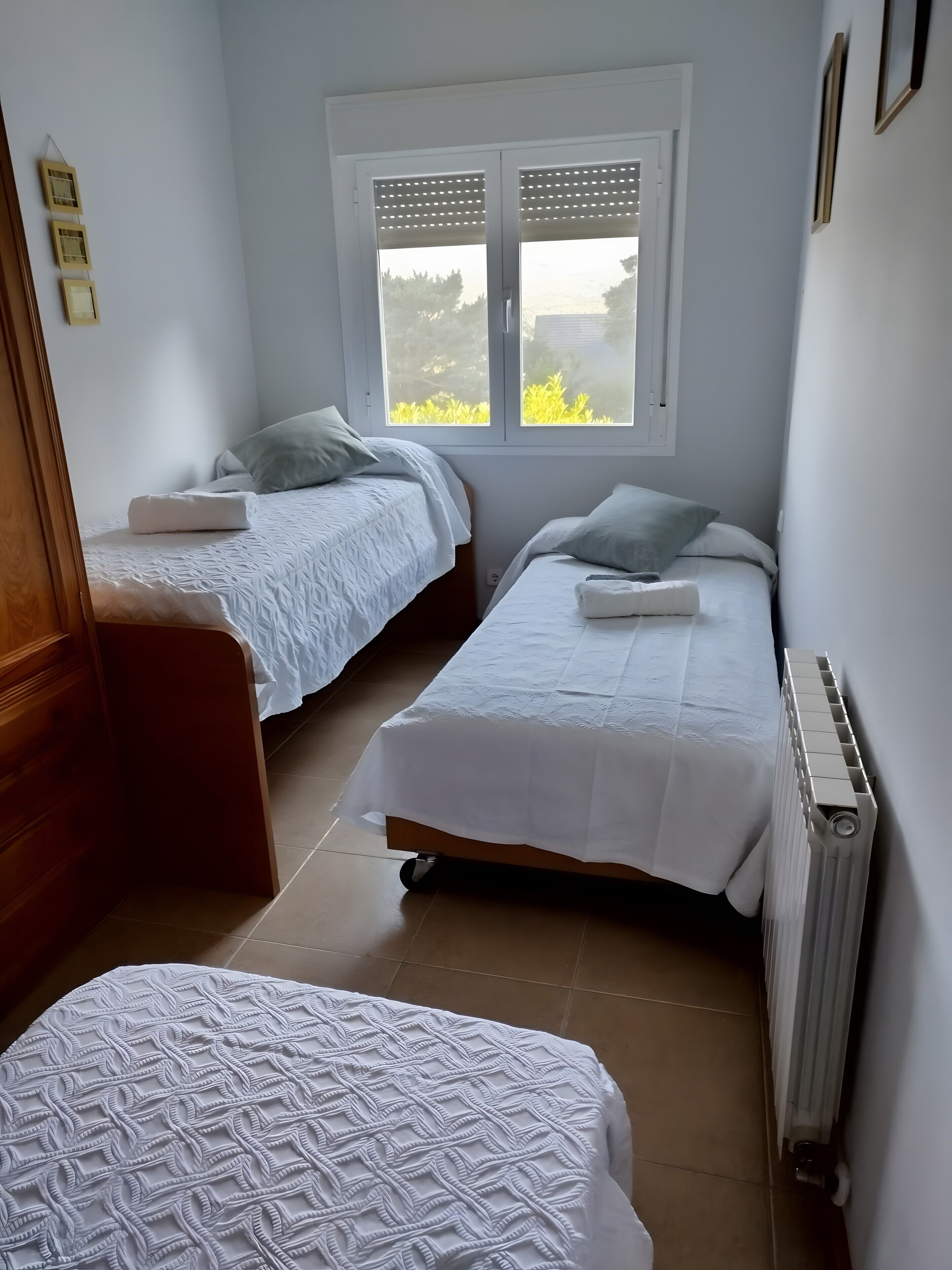 A bedroom with two beds, a window with blinds, a radiator, and a wooden dresser.