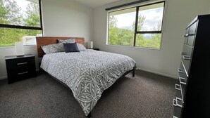 A bedroom with a bed, nightstands, a dresser, and large windows offering a view of trees.
