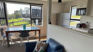 A modern living room with a glass table, two chairs, a blue sofa, and a view of a fenced outdoor area.