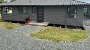 A small, single-story house with a metal roof, a front porch, and a potted plant.
