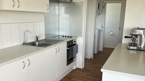 A modern kitchen with white cabinets, a stainless steel sink, a built-in oven, and a coffee machine.
