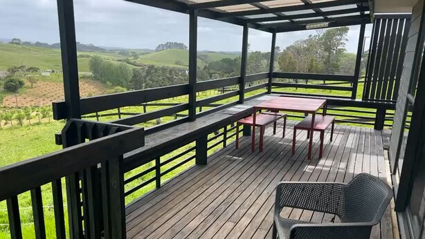A covered outdoor deck with a wooden floor, metal railings, and a table with chairs.