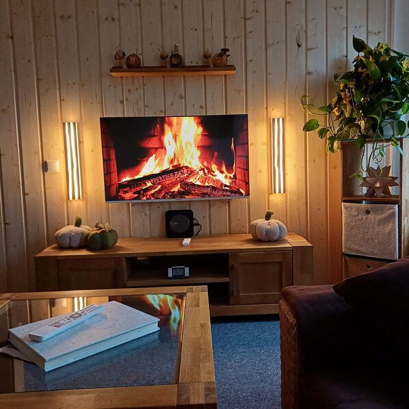 A living room with a flat-screen TV mounted on a wooden wall, a fireplace, and a plant.