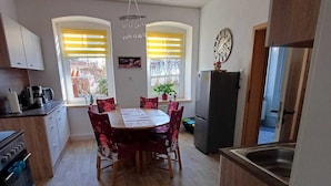A compact kitchen with a dining table, chairs, a refrigerator, and a clock on the wall.