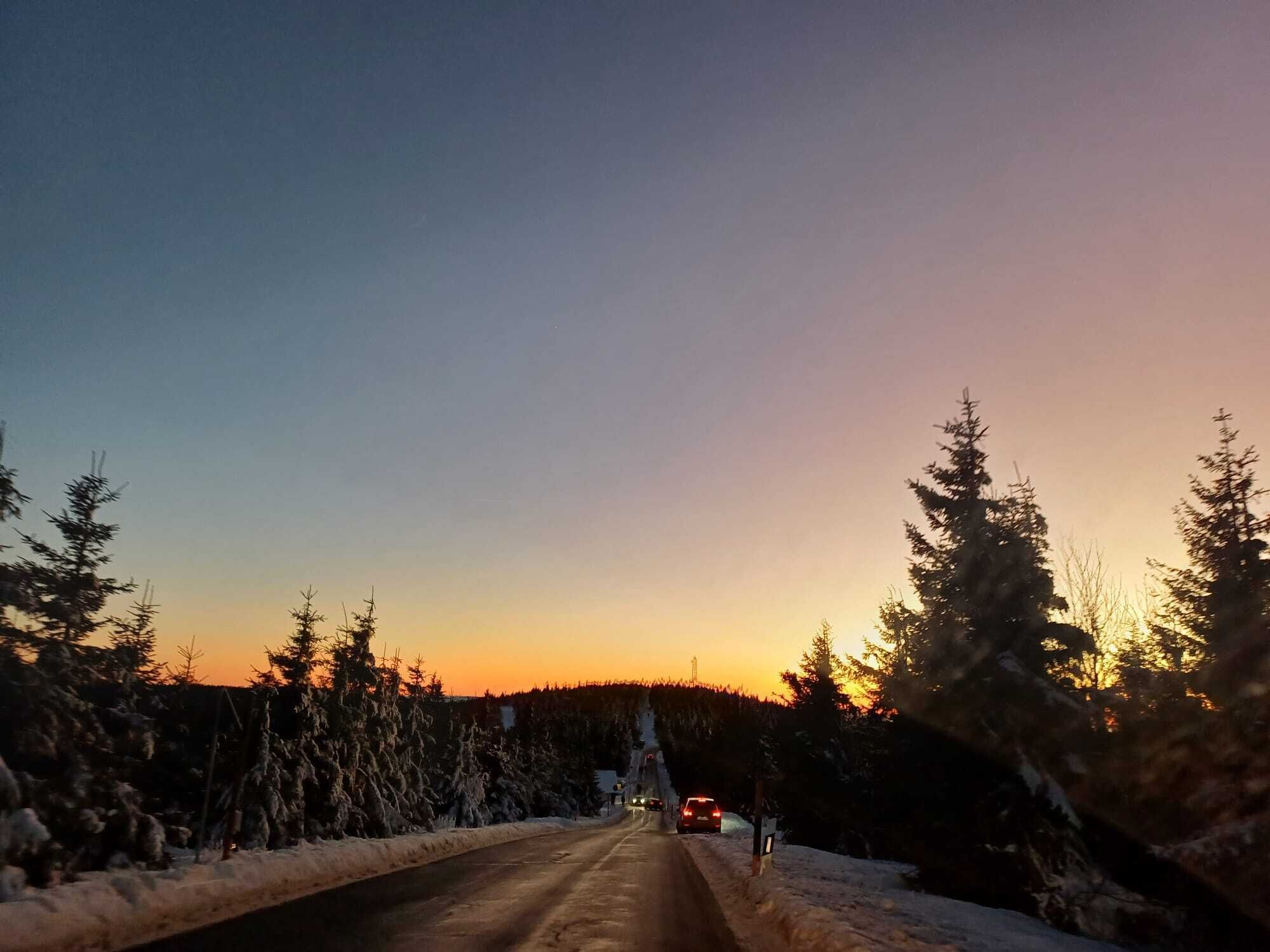 A snow-covered road flanked by evergreen trees under a clear sky.