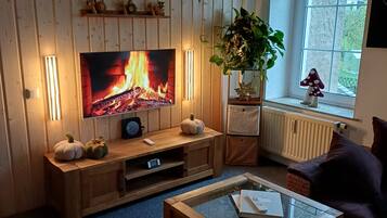 Un salon équipé d’un téléviseur, avec des murs recouverts de panneaux en bois, une plante en pot, une fenêtre offrant une belle vue et une table basse en verre.