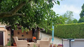 A wooden deck with wicker furniture, a hanging chair, and potted plants.