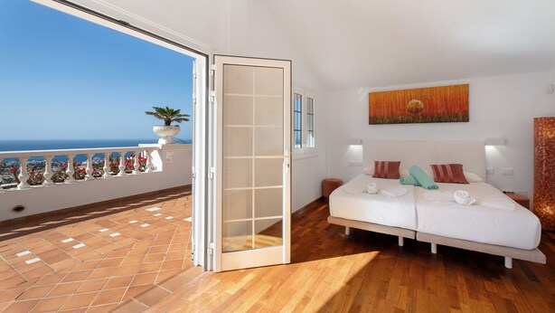 Una camera da letto con balcone, un letto con cuscini e asciugamani, un quadro appeso al muro e una pianta in vaso.