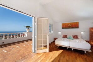 A bedroom with a balcony, a bed with pillows and towels, a painting on the wall, and a potted plant. - Holiday Villa 'Marbella-Heated Private Pool' with Sea Views (Adeje)