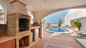 Zona patio con camino in mattoni, piscina, poltrona relax e vista sulla città.