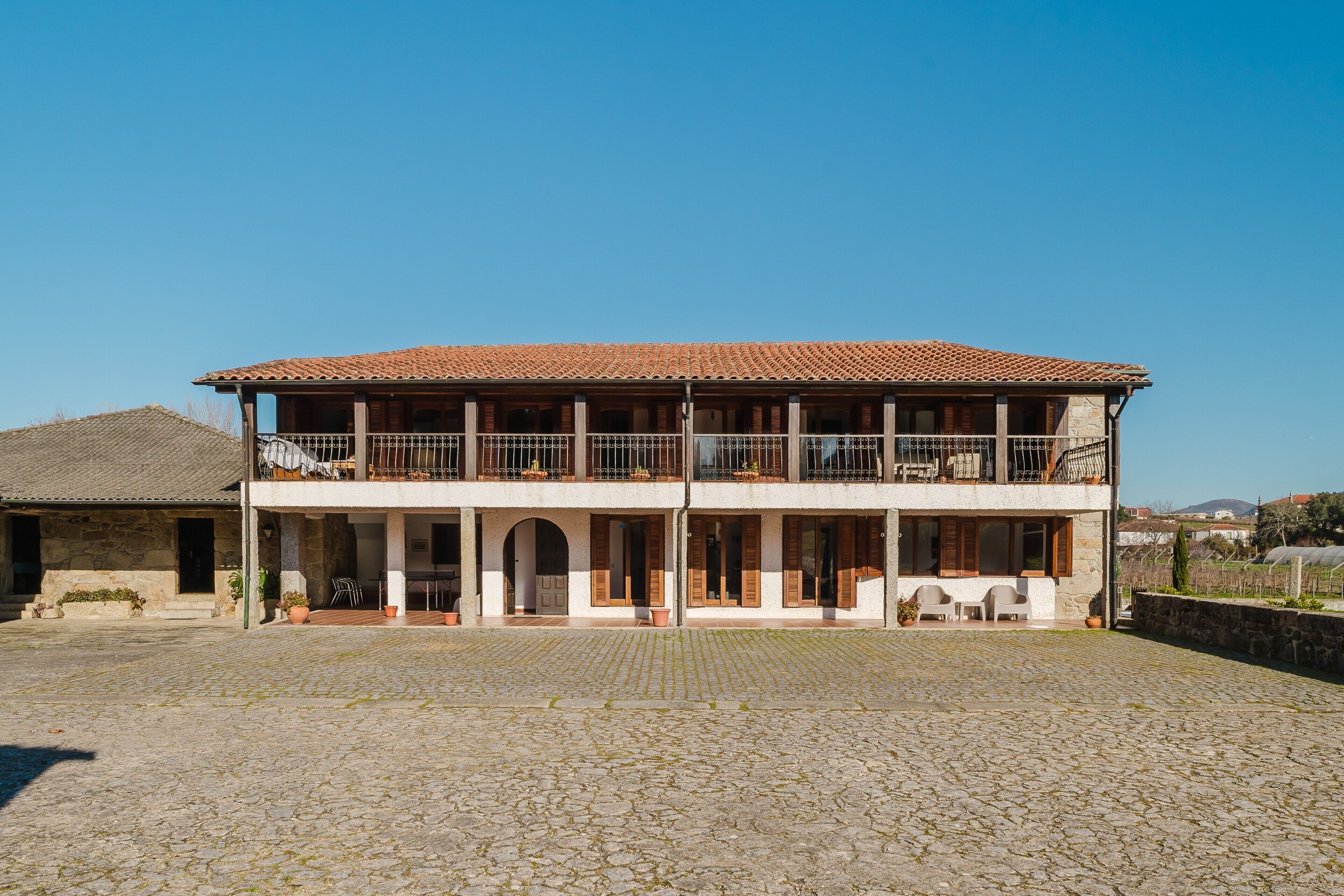 Un bâtiment à deux étages, doté d’un toit en tuiles, d’un patio couvert et d’une cour pavée.