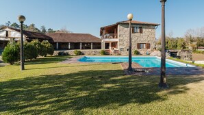 Una casa in pietra su due piani con piscina, immersa in un prato curato e alberi.