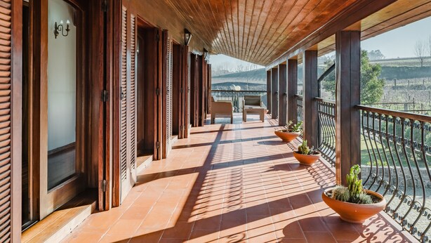 Un balcone coperto con travi in legno, piante in vaso e vista sulla campagna.