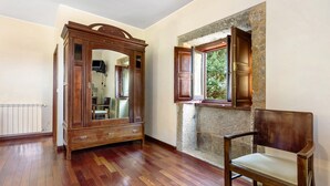 Une pièce avec un plancher en bois, un grand meuble-miroir, une chaise en bois et un mur en pierre avec une fenêtre.