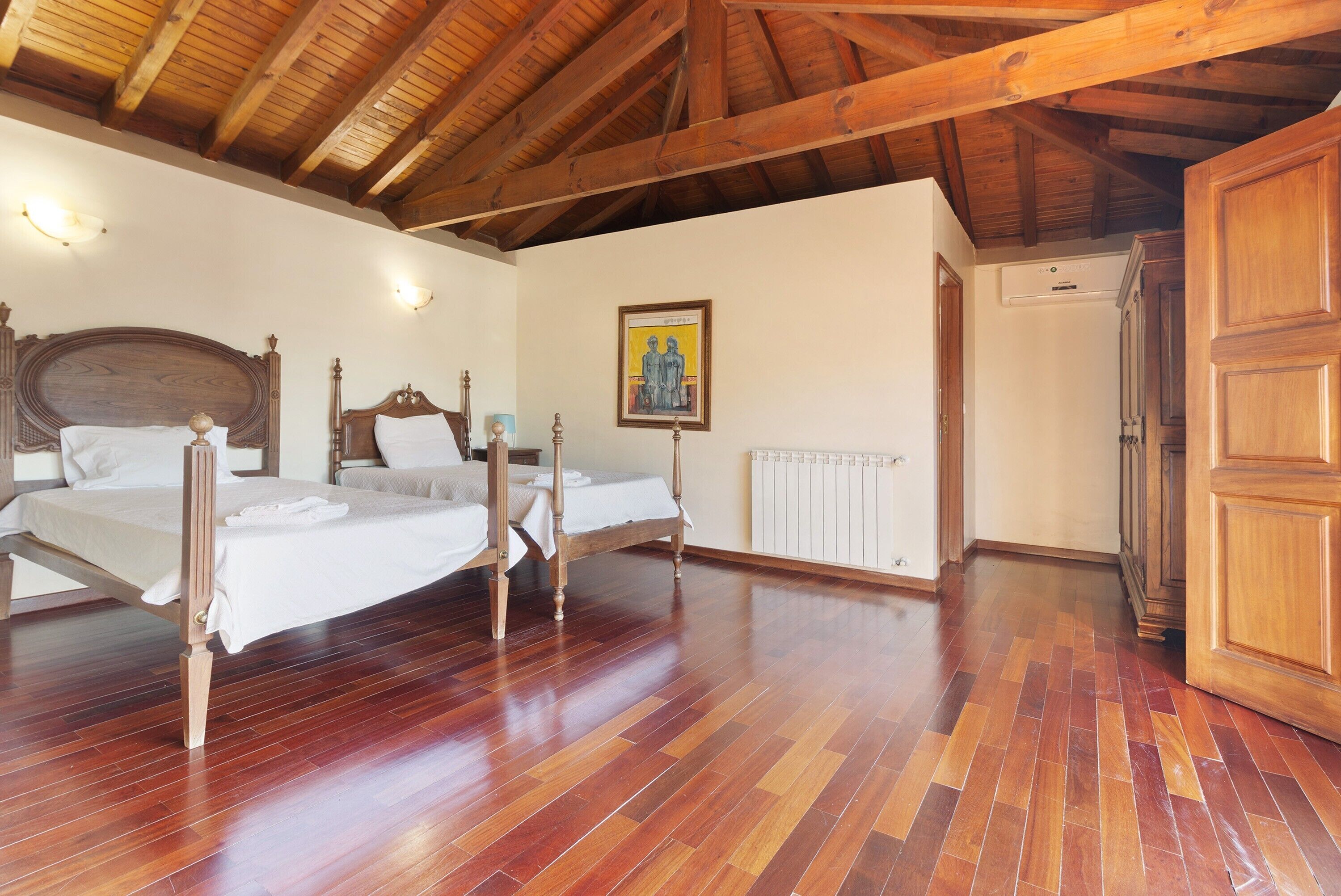 A room with two wooden beds, a radiator, a wooden door, and a framed picture on the wall.