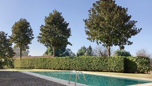 Une piscine dotée d’une terrasse dallée, entourée de haies bien entretenues et de grands arbres.