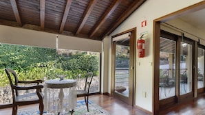 Une pièce avec un plafond en bois, un extincteur, une porte en verre et une vue sur la verdure à l’extérieur.
