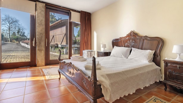 Une chambre à coucher avec un lit en bois, une table de chevet, une lampe et une vue sur l’extérieur, accessible par une porte-fenêtre coulissante.