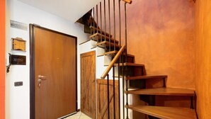 A wooden staircase with a handrail, a closed door with a handle, and a wall-mounted light switch.