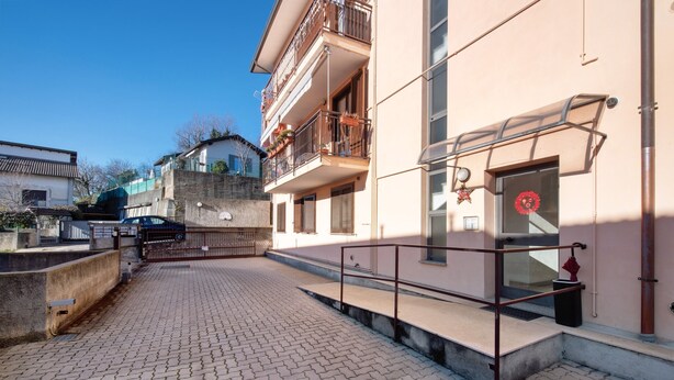 A paved courtyard with a metal railing, a building with balconies, and a clear sky.