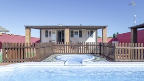 A swimming pool with a wooden fence, a small building with a door, and a clear blue sky.