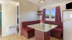A room with a wooden bench, a table with a vase of flowers, a window with curtains, and a white refrigerator.