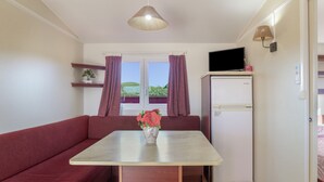 A compact kitchenette with a refrigerator, a dining table with a vase of flowers, a sofa, and a window with curtains.